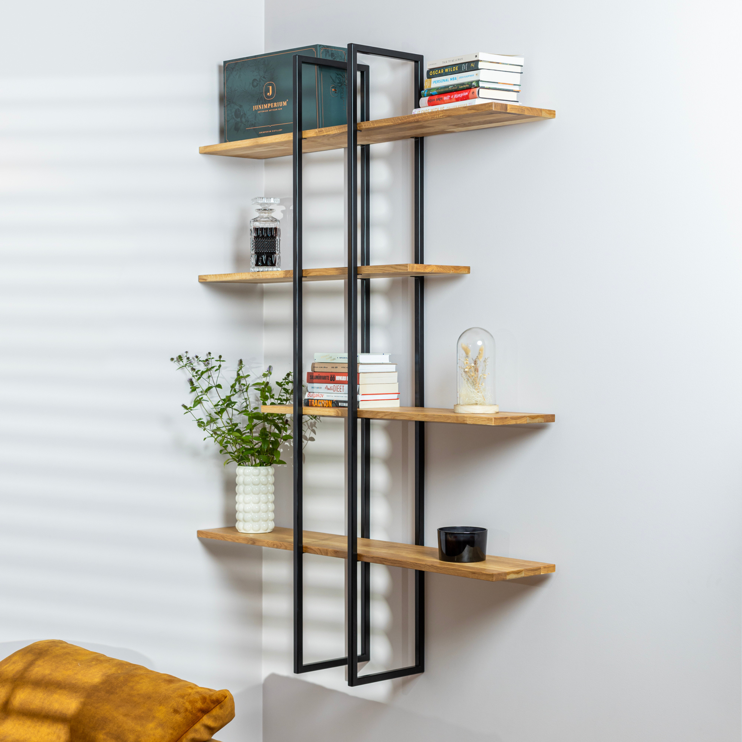 Solid wood floating shelf ÄIKE with two metal frames on a living room wall decorated with a plant, books and a candle