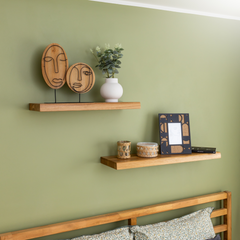 Solid wood floating shelves TUUL on a green bedroom wall decorated with a plant, candle and a photo frame. 