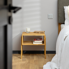 Solid wood bedside table KUU in a bedroom decorated with books on the lower shelf and a candle on the top