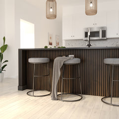 Chocolate brown solid wood acoustic panels attached to a kitchen counter wall. Kitchen in the background and metal legged bar chairs in front of the counter