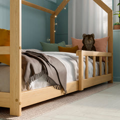 Side view of the Solid wood Montessori House bed with barriers in a modern kid bedroom decorated with pillows, toys and fairy lights