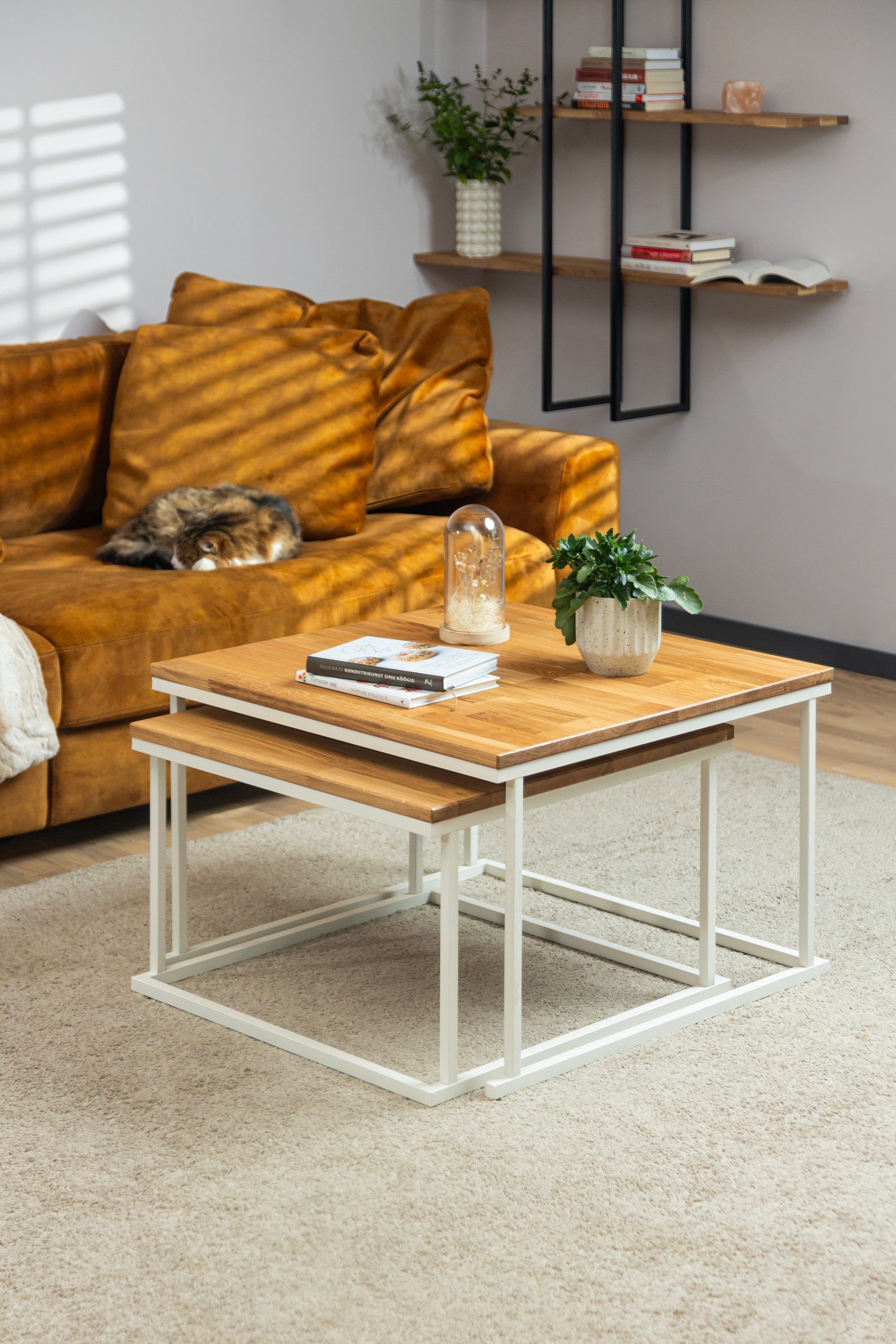 The Nurmenukk coffee table set stacked onto each other and styled with books and a flower for a cozy living room setting