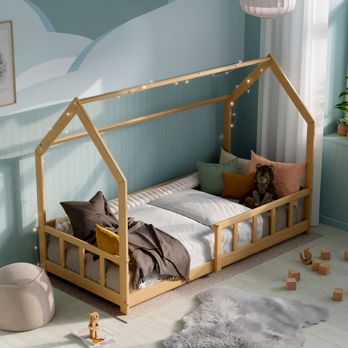 Lit Montessori en bois massif avec barrières dans une chambre d'enfant moderne décorée avec des coussins, des jouets et des guirlandes lumineuses.