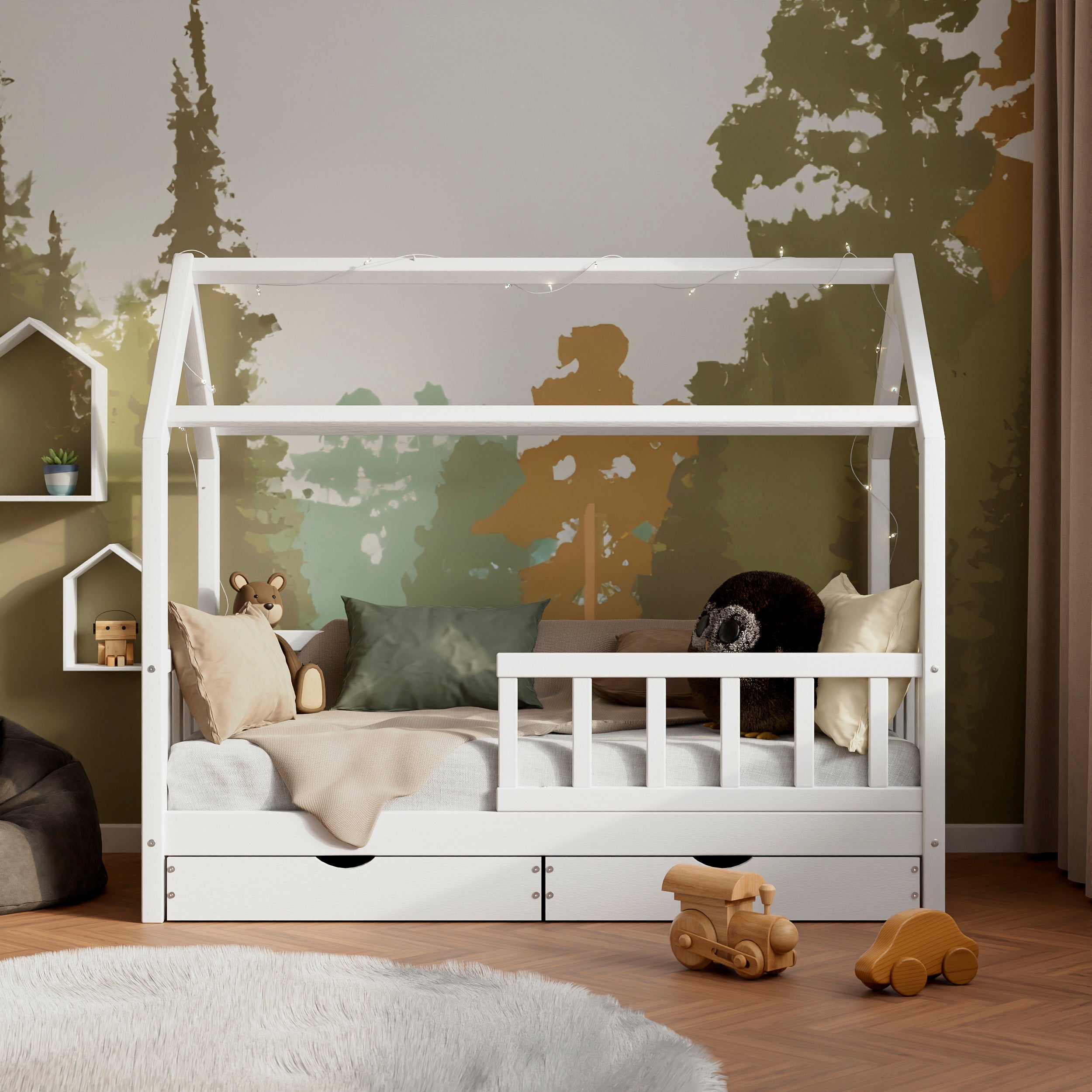 Vue de face du lit maison en bois blanc avec barrières et tiroirs ÖÖBIK avec deux tiroirs dans une chambre d'enfant moderne décorée avec des coussins et des jouets.